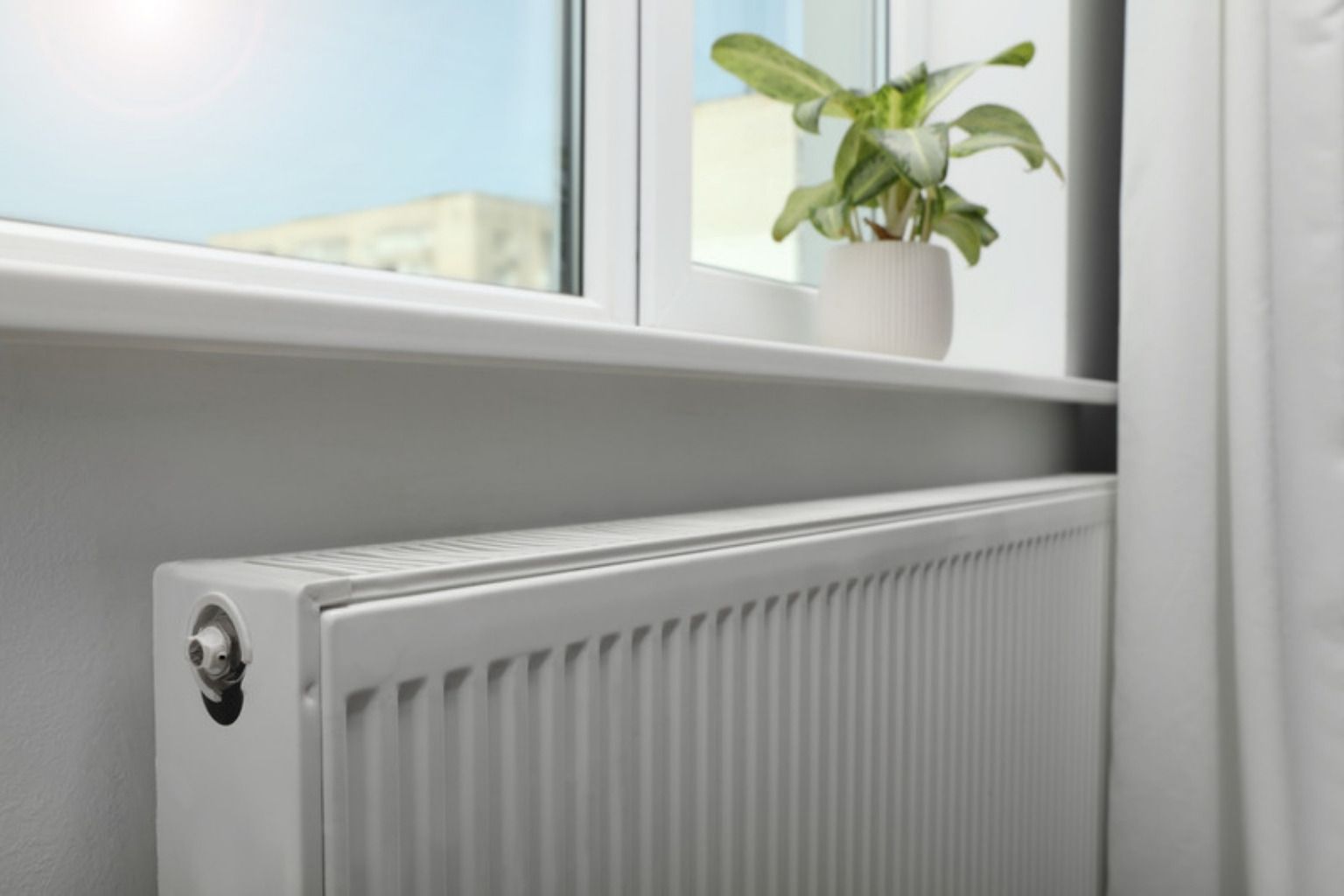 Hvid panelradiator under et vindue med en potteplante i vindueskarmen
